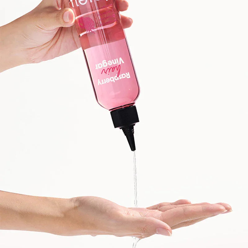 Hand pouring clear raspberry hair vinegar from pink bottle onto palm