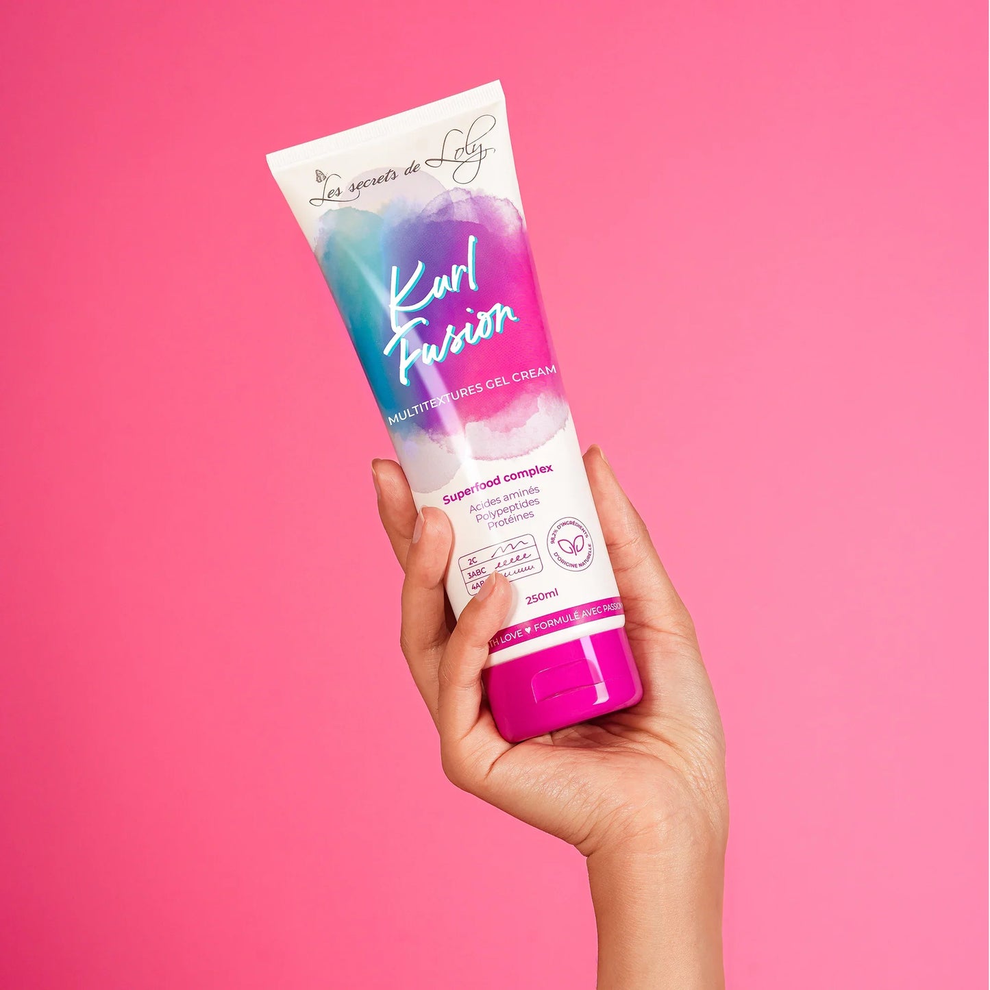 Hand holding a tube of Kurl Fusion multi-textures gel cream against pink background