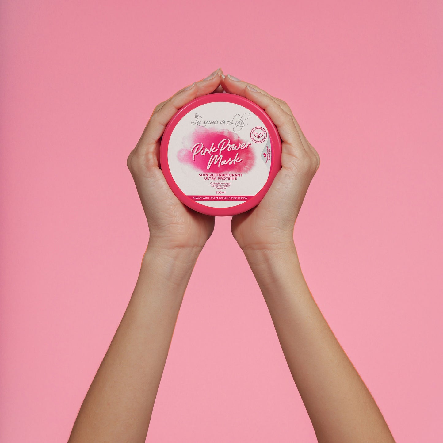 Hands holding Pink Power Mask hair treatment jar against a pink background.
