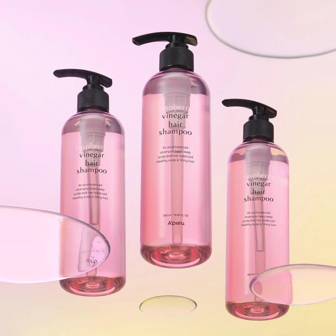 Three bottles of raspberry vinegar hair shampoo with pink liquid and black pumps on a pastel background