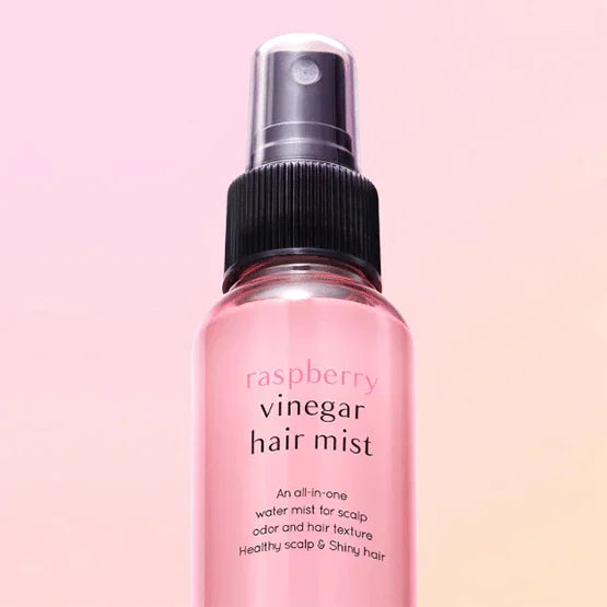 Raspberry vinegar hair mist spray bottle with pink liquid on a soft pink gradient background