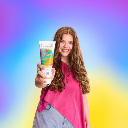 Smiling woman with long curly hair holding cream conditioner tube on colorful gradient background