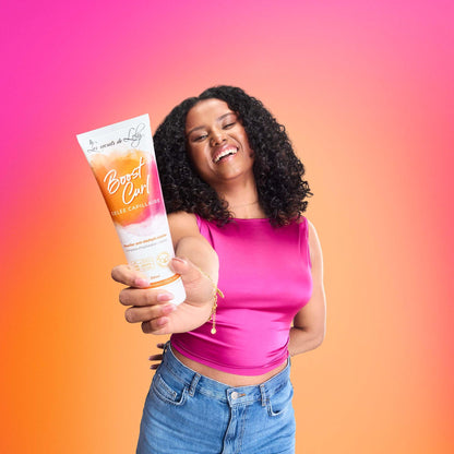 Smiling woman holding Boost Curl hair gel against a vibrant pink and orange background