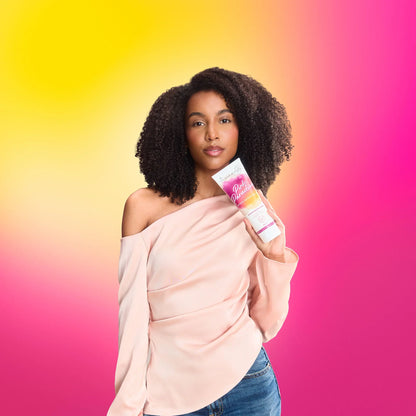 Woman with curly hair holding hair care product against pink and yellow gradient background