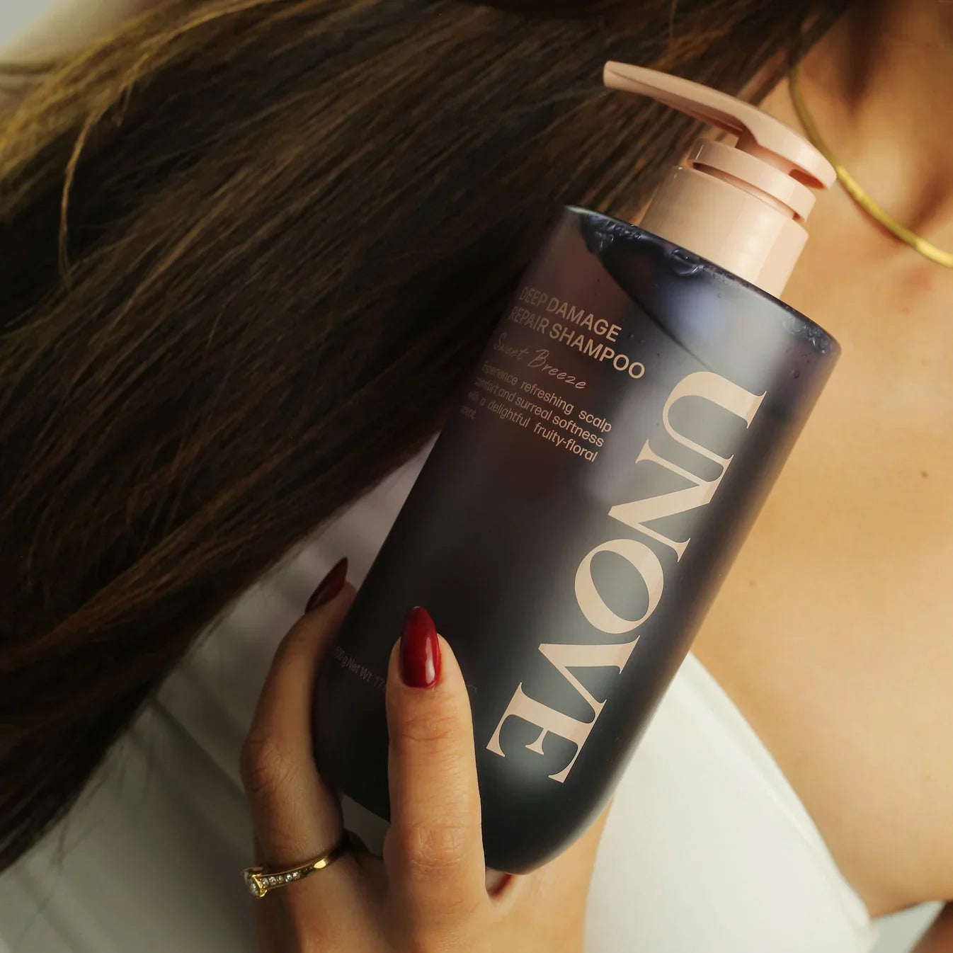 Woman holding Unove Deep Damage Repair Shampoo bottle near long brunette hair