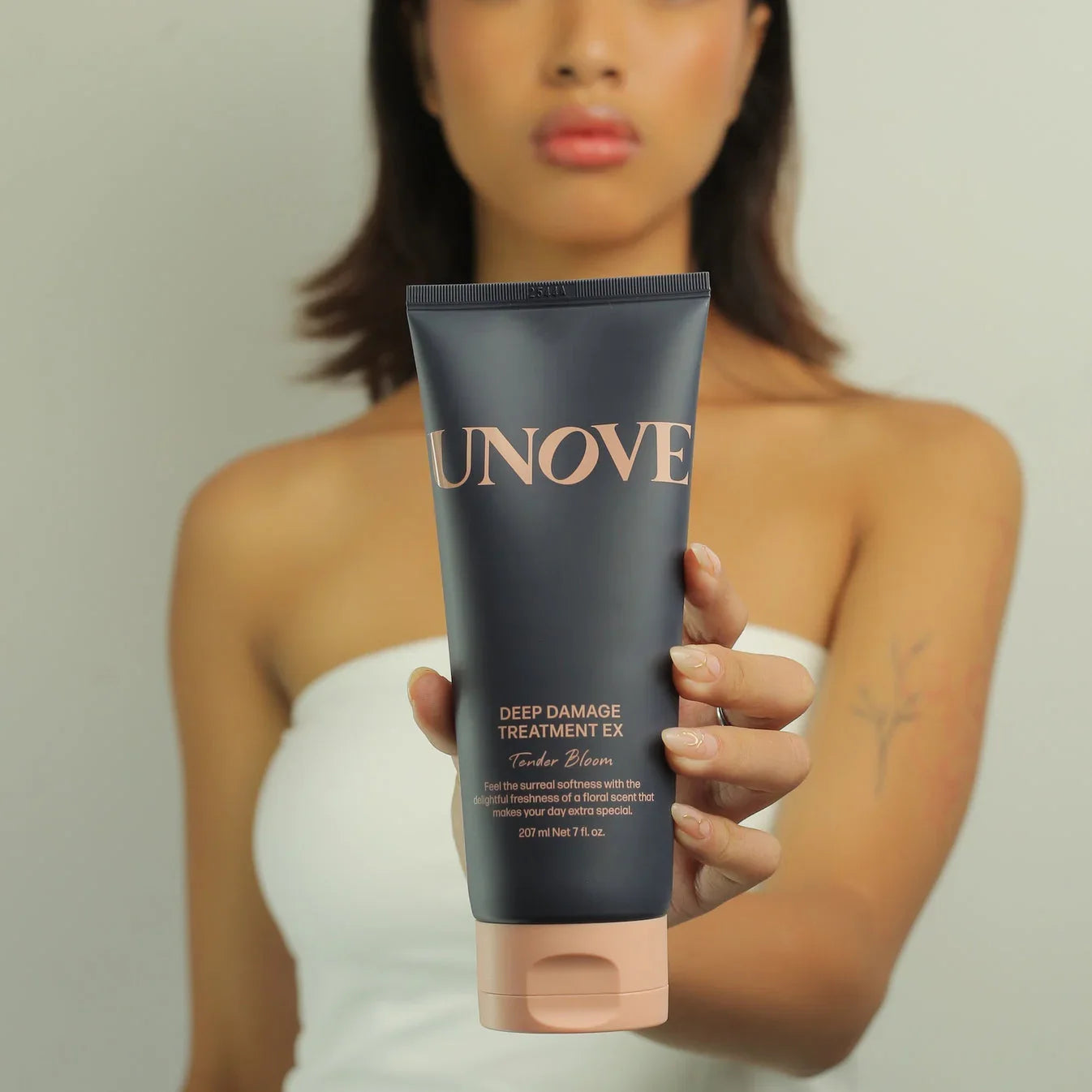 Woman holding UNOVE Deep Damage Treatment EX hair care product in front of her