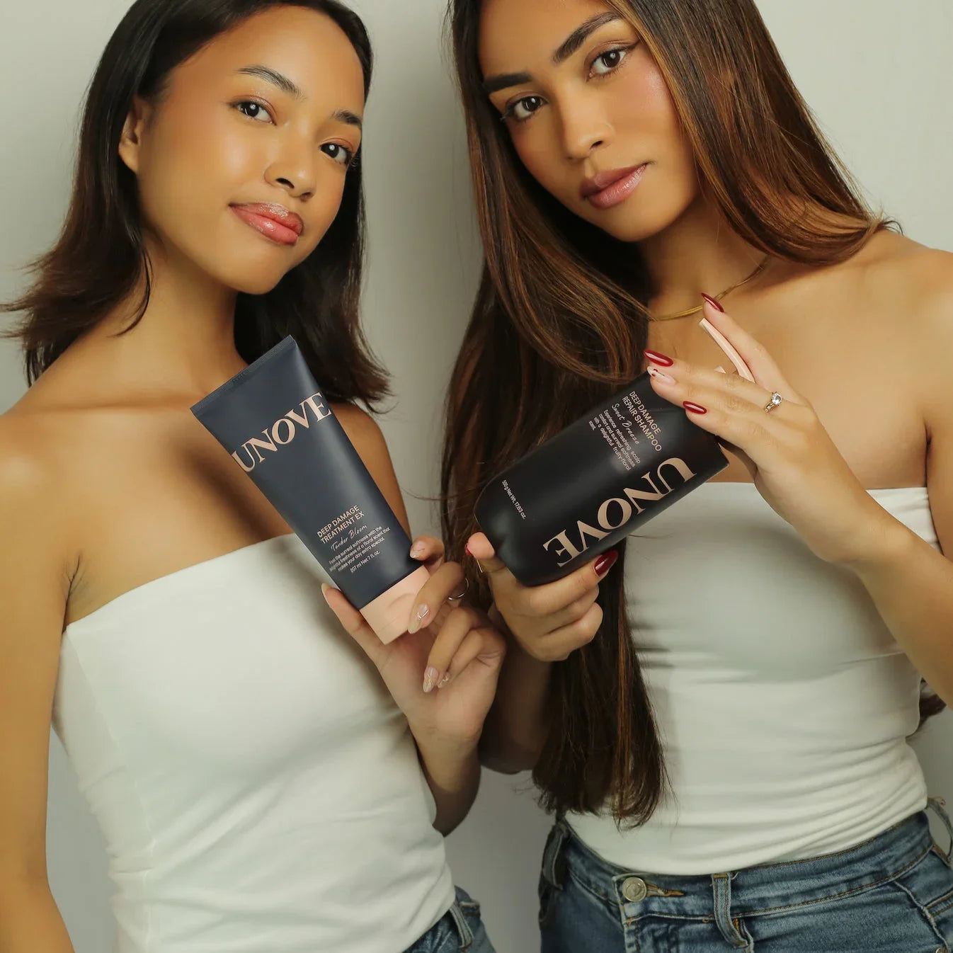 Two women in white tops holding Unove hair care products against a neutral background