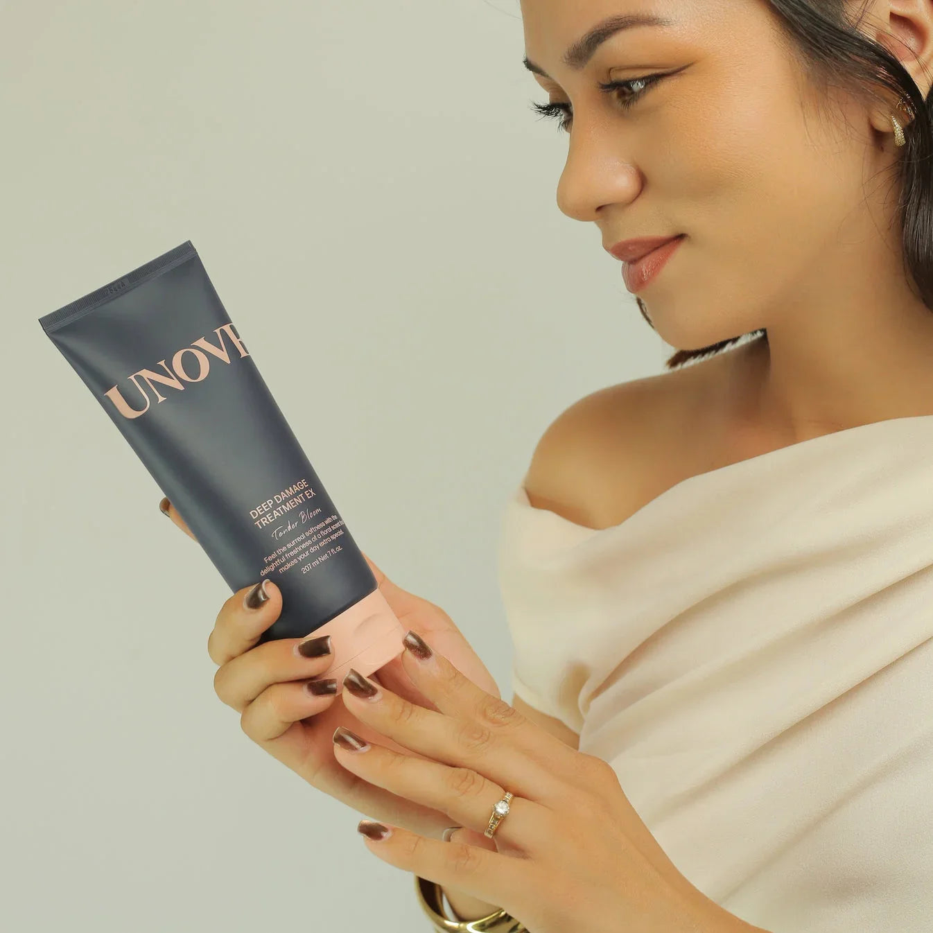 Woman holding Unove deep damage hair treatment tube against light background