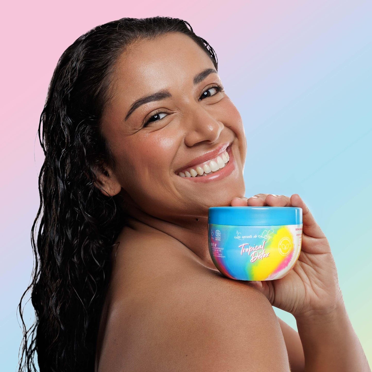Smiling woman with wet hair holding a colorful Tropical Detox hair care product jar