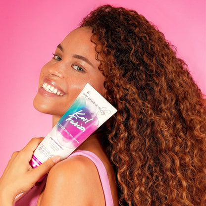 Smiling woman with curly hair holding curl fusion gel cream against pink background