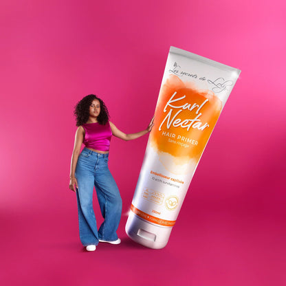 Woman with curly hair standing next to oversized Kur! Nectar hair primer tube on pink background