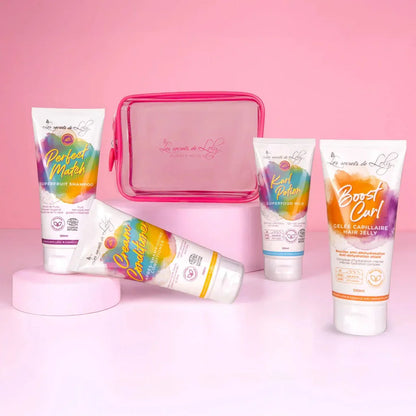 Hair care travel kit with colorful shampoo, conditioner, curl milk, and hair jelly tubes on pink background