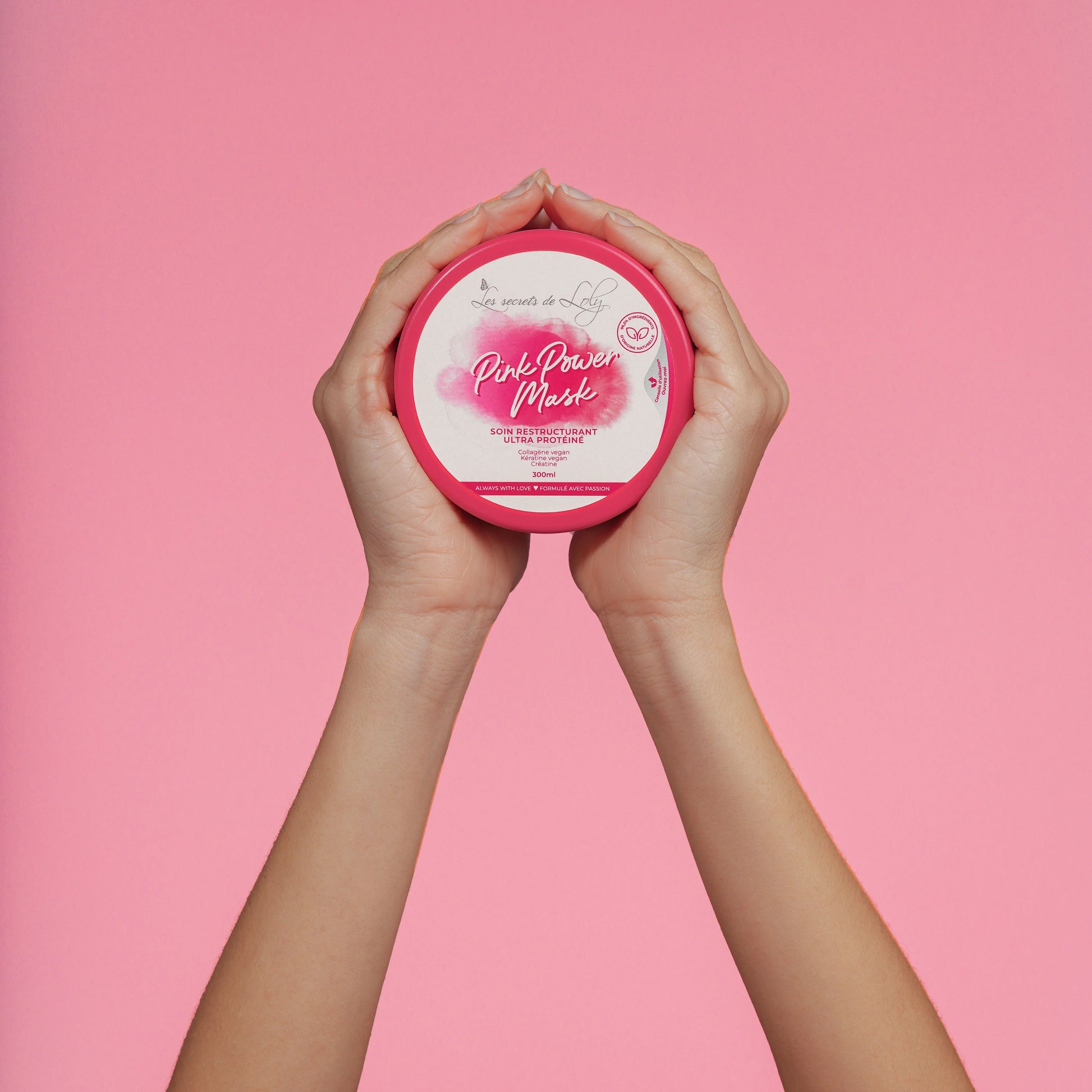 Hands holding Pink Power Mask hair treatment jar against a pink background.