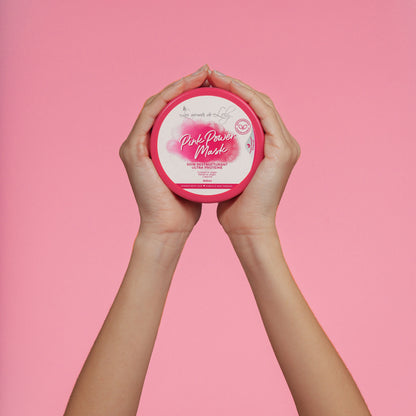 Hands holding Pink Power Mask hair treatment jar against a pink background.