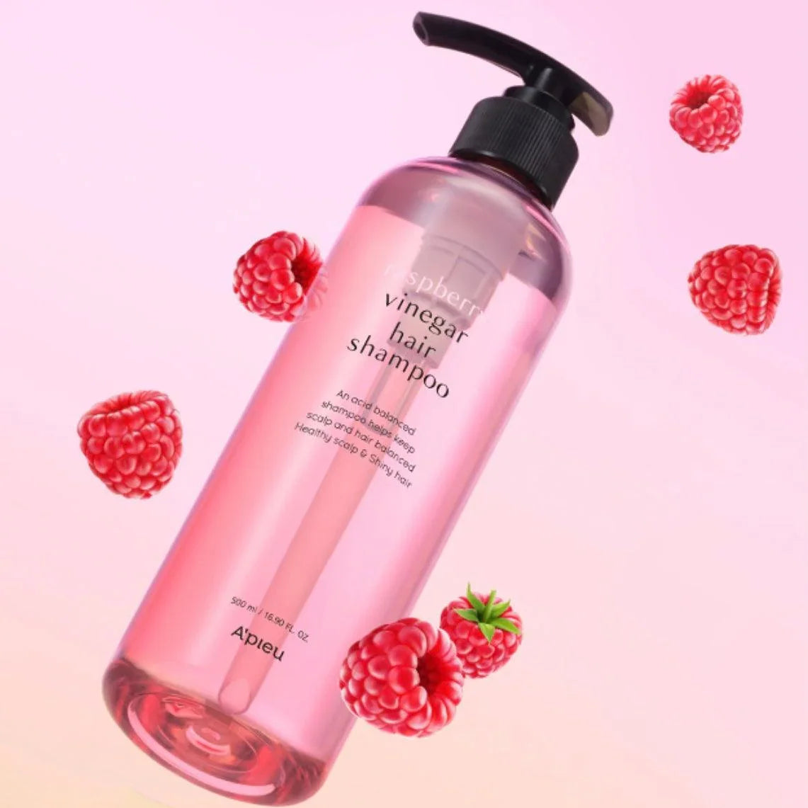 Pink bottle of raspberry vinegar hair shampoo with pump surrounded by fresh raspberries on a gradient background