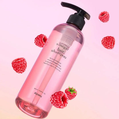 Pink bottle of raspberry vinegar hair shampoo with pump surrounded by fresh raspberries on a gradient background