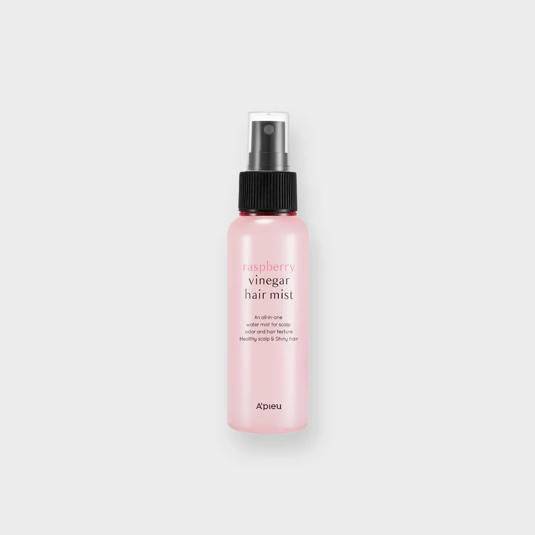 Pink bottle of raspberry vinegar hair mist with black spray cap on white background.